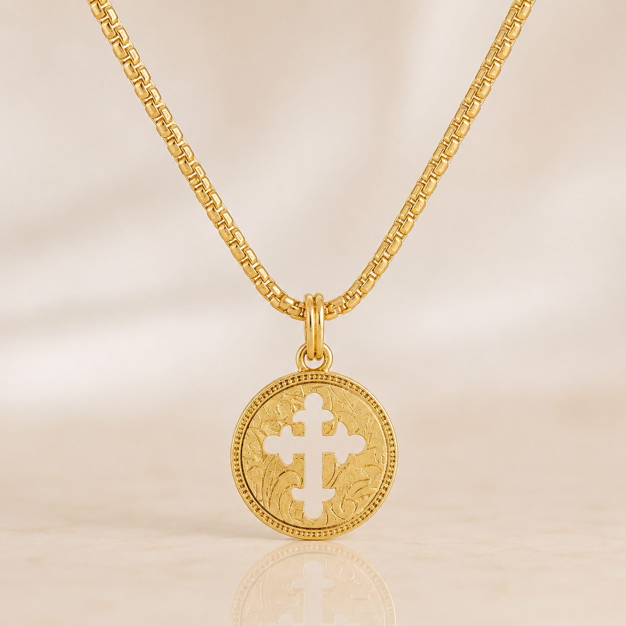 A gold chain necklace with a round gold pendant featuring a white cross in the center, displayed on a light beige background.