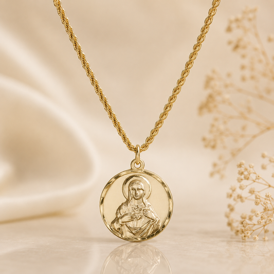 A gold necklace with a round medallion pendant featuring an embossed religious figure, displayed on a soft beige satin surface with dried flowers in the background.