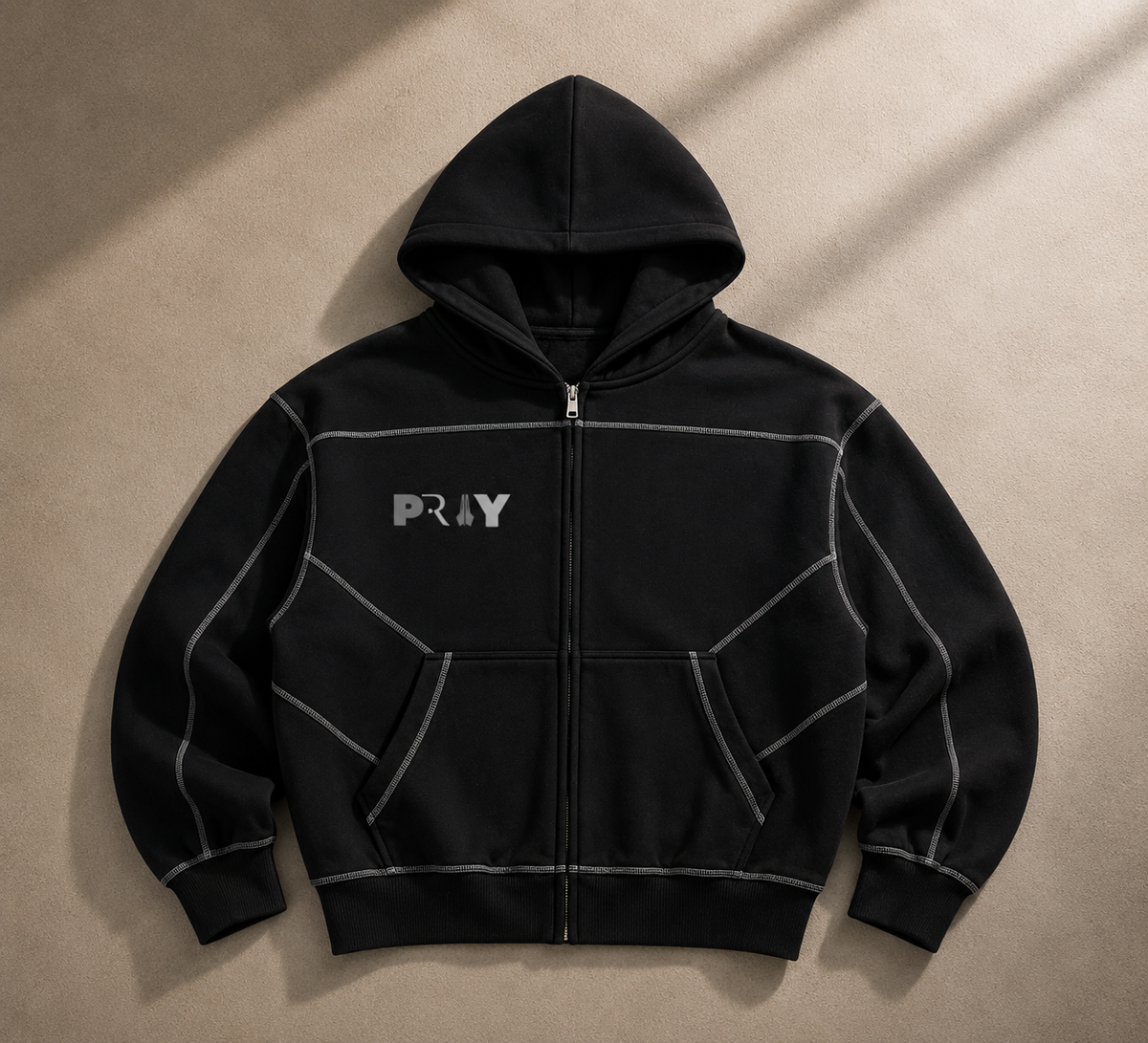 A black zip-up hoodie with a full front zipper, hood, and kangaroo pockets, featuring a silver 'PLAY' logo on the left chest and contrasting light gray stitched panel lines. The hoodie is laid flat on a textured beige background with diagonal shadows.