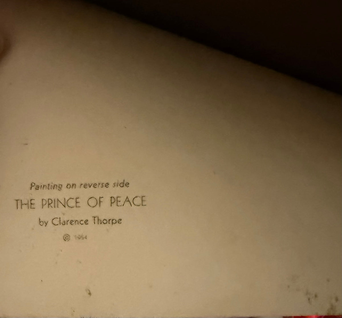 A close-up of a beige paper surface with handwritten text reading 'Painting on reverse side THE PRINCE OF PEACE by Clarence Thorpe © 1964'.